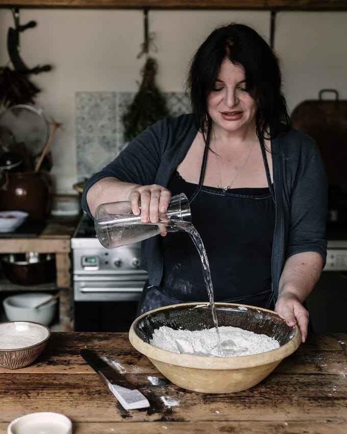 Teaching you to bake the healthiest bread in the world - Sourdough Hydration as bread Expert Vanessa Kimbell hydrates her bread pouring water onto flour in a bowl at the table