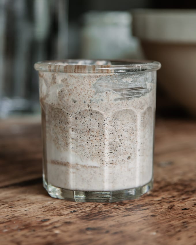 Sourdough starter in a glass jar on a wooden table. Acetic acid in sourdough