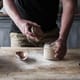 A with a glass jar in his hands with sourdough starter inside, placed on a wooden table.