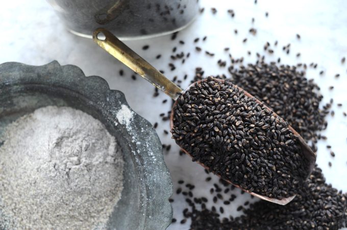 black barley grains in a gold spoon with grains overflowing onto the table.