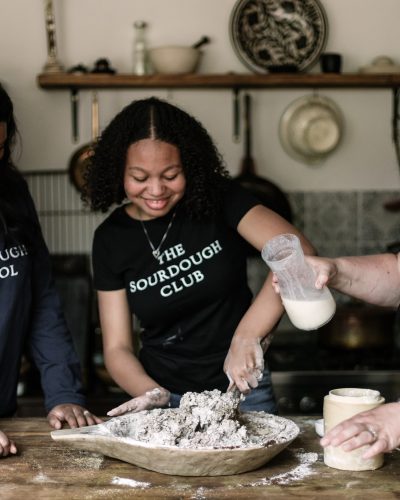 Two young women and Vanessa Kimbell mixing a bread dough.