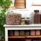 Glass jars of a variety of differnent beans and gains sit on wooden shelves in bright daylight.