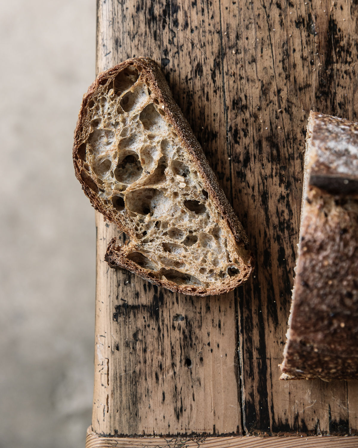 A close up of a slice of crusty soudough is on top of a rustic wooden table