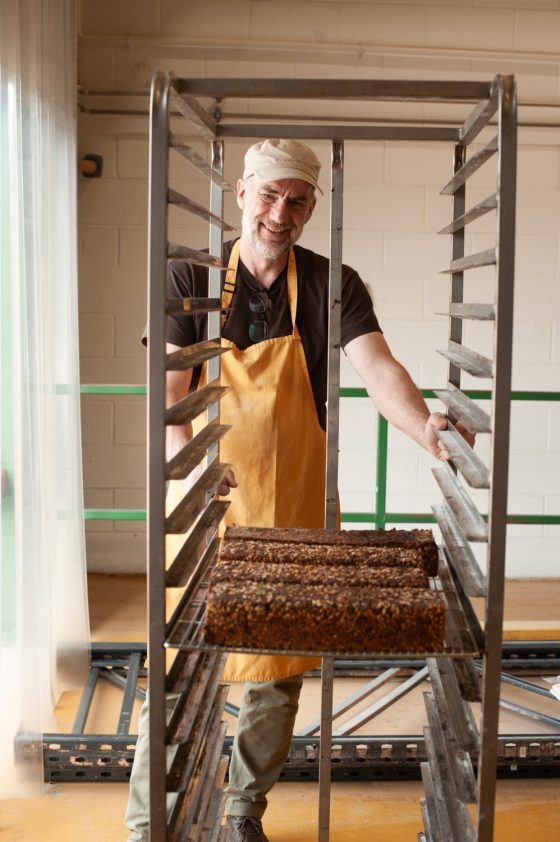 Baker stands with the proven bread on a bakery rack