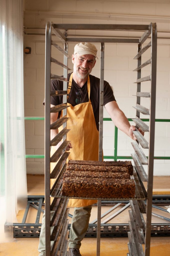 Baker đứng với bánh mì đã được chứng minh trên giá bánh