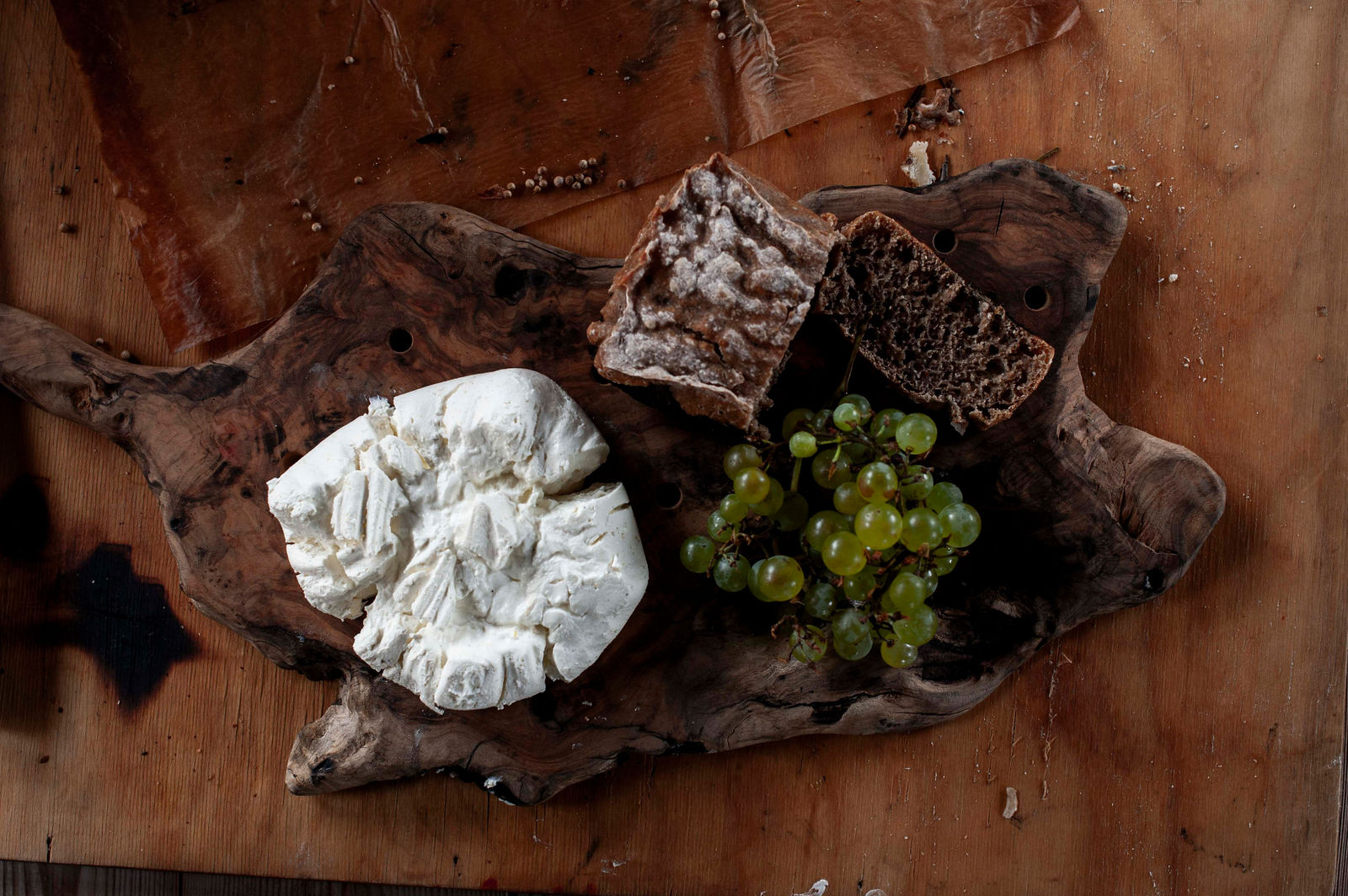 Cheese, sourdough and grapes on top of a wooden board.